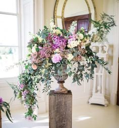 a vase filled with lots of flowers on top of a wooden table next to a mirror