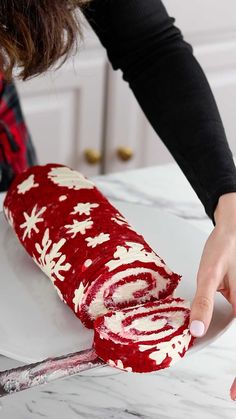 a woman is decorating a roll with red and white frosting on the counter