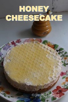 a cheesecake sitting on top of a floral plate next to a honey shaker