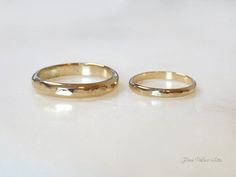 two gold wedding rings sitting on top of a white table