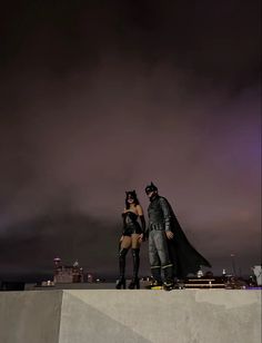 two people dressed as batman and catwoman standing on top of a ramp at night