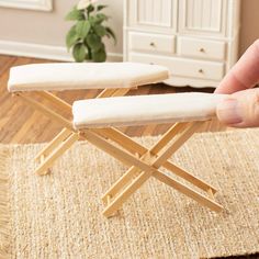 a hand is holding the top of a wooden folding bench on a rug in front of a white dresser