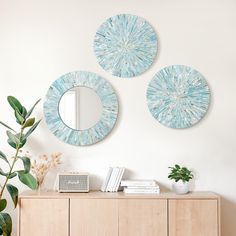 three circular mirrors mounted on the wall above a wooden sideboard with books and plants