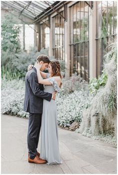 an engaged couple embracing in front of a greenhouse