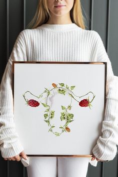 a woman holding up a framed painting with flowers on it