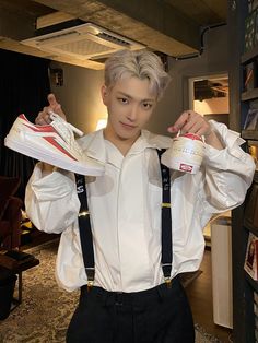 a man in suspenders holding up two pairs of shoes and one pair of sneakers