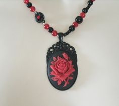 "Red Rose Necklace This beautiful necklace has red glass beads, black glass beads, seed beads, black metal connectors with rhinestones, black metal chain and a black metal pendant with resin rose. 20\" long. Lobster clasp." Gothic Beaded Necklace For Gift, Vintage Black Necklace For Valentine's Day, Gothic Rose Jewelry For Gift, Gothic Rose-colored Jewelry For Gifts, Gothic Rose Colored Jewelry For Gift, Rose-colored Gothic Jewelry For Gift, Gothic Black Bead Necklace For Gift, Gothic Black Beads Necklace For Gift, Adjustable Gothic Beaded Necklace As Gift