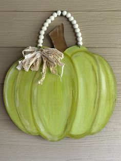 two green pumpkins are hanging on the wall with beaded necklaces around them