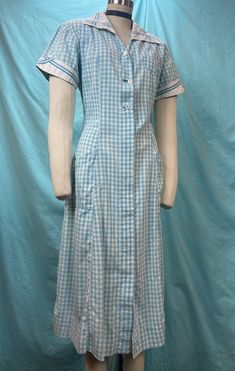 "1940s W:35 Angelica vintage uniform dress pockets gingham plaid blue aqua short sleeve button up collared V neck A-line skirt shirtwaist Great 40s uniform dress for Angelica. A-line silhouette of paneled construction with seams falling from the shoulder. Button down with some mismatched white buttons. Fully opens up. Two slanted side pockets and one side pocket. Cotton fabric in sweet shade of vintage blue aqua contrasted with white on sleeves cuffs and neckline. Photographed on fitting form size 2, check measurements, vintage size labeled 36. MEASUREMENTS  Bust: 40\" Waist: 35\" Hips: 40\" Length: 45\" with 2 1/2\" hem available This is in good vintage condition, there's a few small pin holes and some light overall wear to cotton. Rip at button hole, some tearing. Some fading throughout. Retro Short Sleeve School Dresses, Short Sleeve Plaid Gingham Dress For Daywear, Short Sleeve Gingham Plaid Dress For Daywear, Vintage Plaid Short Sleeve Dress, Retro Short Sleeve Plaid Gingham Dress, Vintage Gingham Dress With Short Sleeves, Casual Plaid Short Sleeve Dress With Buttons, Casual Short Sleeve Plaid Dress With Buttons, Casual Plaid Dress With Short Sleeves And Buttons