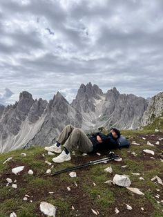 a man laying on top of a lush green hillside next to mountains with rocks and grass