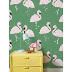 pink flamingos on green wallpaper next to a yellow dresser with a blue lamp