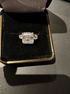 an engagement ring sitting on top of a black velvet box with a white diamond in it