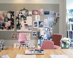 a wooden table topped with pink chairs next to a wall covered in pictures and photos