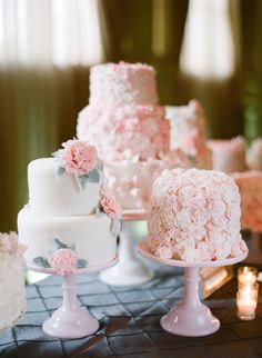 a table topped with three different cakes covered in frosting and pink flowers on top of each cake