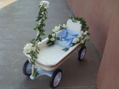 a white baby carriage with flowers and greenery on the front wheel, sitting in front of a building