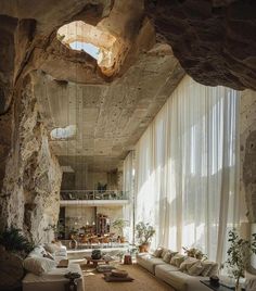 a living room filled with lots of furniture next to a stone wall and window covered in sheer curtains