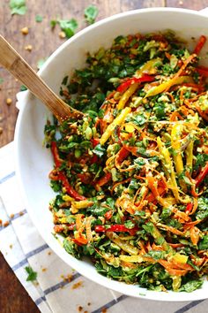 a white bowl filled with colorful salad on top of a wooden table next to a napkin