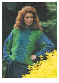 a woman wearing a green and blue sweater standing in front of yellow flowers with her hands on her hips