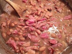 beans and ham are being cooked in a pot with a wooden spoon on the side