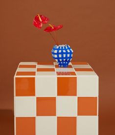 an orange and white checkered table with a blue vase holding two red flowers on it