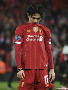 a young man in a red uniform standing on a soccer field with his head down