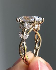 a close up of a person's hand holding a gold ring with an oval shaped diamond