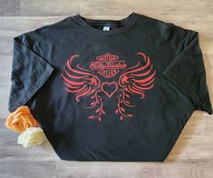 a black long sleeve shirt with an orange flower on the left side and a red design on the right