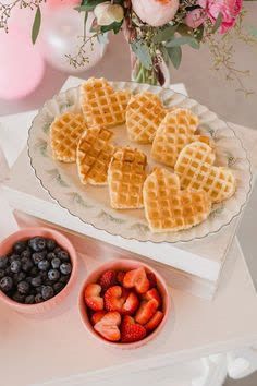 waffles, berries and blueberries on a table with pink flowers in the background