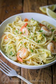 a white bowl filled with pasta and shrimp on top of a wooden table next to a fork