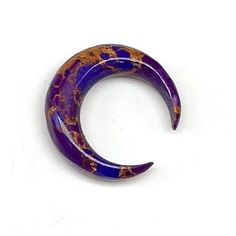 a purple and gold crescent brooch sitting on top of a white surface