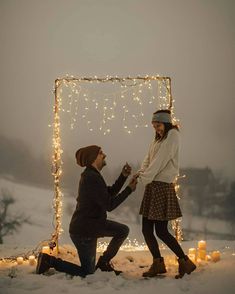 two people kneeling down in the snow with lights around them and candles on the ground