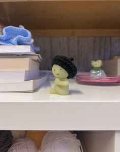 there is a small doll sitting on the shelf next to some yarns and crochet