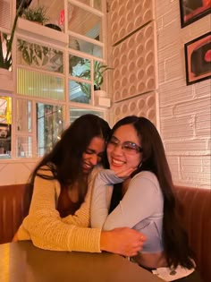 two women sitting at a table hugging each other