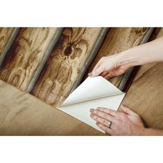 a woman is holding a piece of paper on top of a wooden table with wood planks in the background