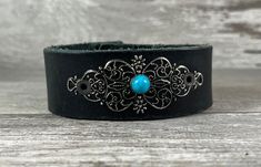 This narrow distressed black leather cuff features a vintage inspired filigree embellishment that was hand painted for a rich patina look, then fastened to the cuff with a domed faux turquoise rivet. The strap shows wonderful wear and distress marks that add to the character of the piece - these are not defects! Check alternate photos to view. Like all genuine leather goods, the cuff will continue to soften and become more pliable with every wear. Also, I use quality heavy-duty snaps which will seem tight at first, but will loosen a bit with wear. SIZING: The bracelet is adjustable with two snaps, should comfortably fit up to a 7" wrist. Not sure what size your wrist is? Check out this free printable tape measure by cutting and pasting this link into your browser: https://www.inchcalculato Black Cuff Leather Bracelet For Festivals, Black Leather Cuff Bracelet For Festivals, Blue Leather Festival Bracelets, Blue Leather Bracelets For Festival, Black Leather Western Jewelry, Western Black Leather Jewelry, Adjustable Western Leather Bracelet For Festivals, Western Style Black Leather Jewelry, Black Bohemian Leather Bracelet, Adjustable