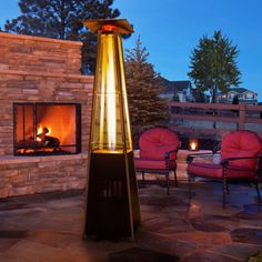 an outdoor fireplace with red chairs around it and a fire pit in the background at night