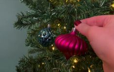 a hand holding a red ornament on top of a christmas tree