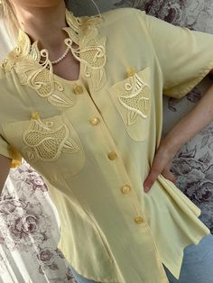 A vintage light yellow blouse adorned with intricate embroidery, offering a soft, feminine charm. This women's short-sleeve shirt features a unique see-through ornament on the back, adding a subtle yet alluring detail. The delicate embroidery and airy design make it a perfect piece for warm weather, combining vintage elegance with a modern, breezy style. - Good vintage condition  - TAG SIZE: no information  - Fabric information: 60% viscose 40% polyester  Estimated to fit XS-S-M-L based on your Cream Short Sleeve Blouse For Summer, Elegant Beige Summer Shirt, Feminine Short Sleeve Cream Blouse, Feminine Cream Short Sleeve Blouse, Summer Embroidered Beige Blouse, Summer Beige Blouse With Floral Embroidery, Beige Blouse With Floral Embroidery For Summer, Embroidered Beige Blouse For Summer, Fitted Beige Blouse For Summer