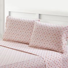 a bed with white sheets and orange polka dot print on the coverlet, in front of a window