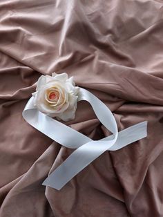 a white rose is sitting on top of a pink satin sheet with a ribbon around it