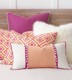 the pillows are lined up on the bed with white and pink accents, along with other decorative items