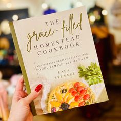 a person holding up a book about the grace - filled homestead cookbook