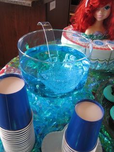 a table topped with plates and cups filled with blue liquid next to a barbie doll