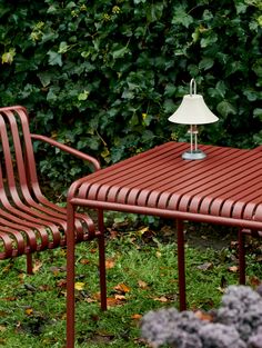 an outdoor table with two chairs and a lamp on it in the grass near some bushes