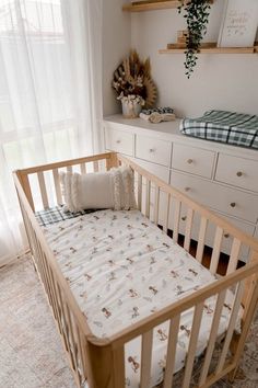 a baby's crib in the corner of a room with white curtains and wooden furniture