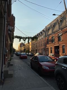 cars parked on the side of a street next to tall brick buildings and power lines