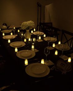 a long table is set with white plates and lit candles in front of the centerpieces