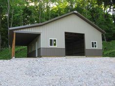 a two car garage sitting on top of a gravel covered hill next to trees and bushes