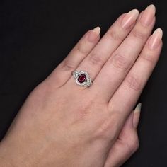 a woman's hand holding a ring with a red stone in the middle and white diamonds around it