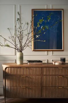 a vase filled with flowers sitting on top of a wooden dresser next to a painting